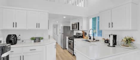 Una cocina moderna con armarios blancos, una isla central, un microondas, una estufa y una cafetera.