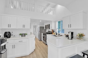A modern kitchen with white cabinetry, a central island, a microwave, a stove, and a coffee machine.