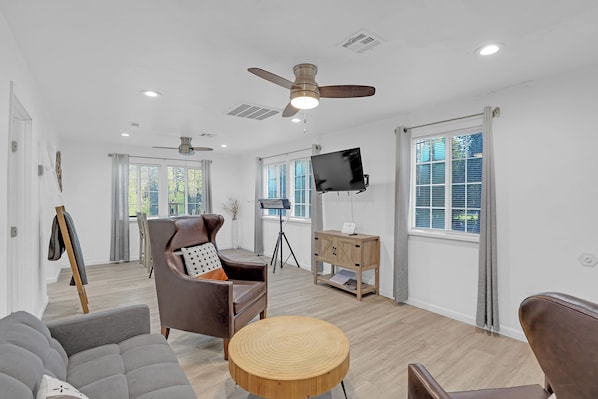 A modern living room with a ceiling fan, a flat-screen TV, and a wooden coffee table.
