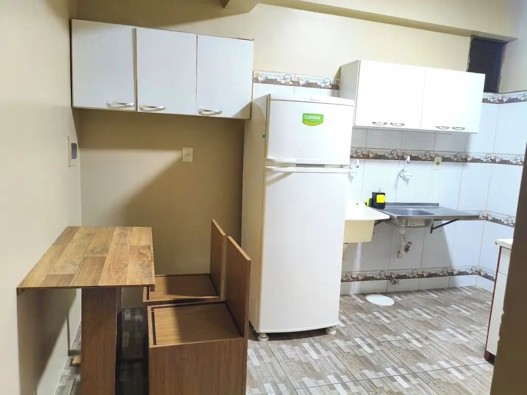 Una cocina compacta con alacenas blancas, un refrigerador, una mesa de madera y un lavamanos.