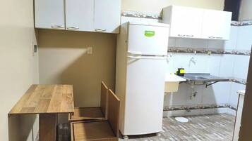 Una cocina compacta con alacenas blancas, un refrigerador, una mesa de madera y un lavamanos.
