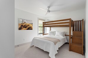 Ein Etagenbett mit Holzrahmen und weißer Bettwäsche, ein Deckenventilator und ein großes Fenster mit Blick ins Freie.