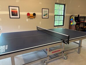 Ein Tischtennis-Tisch mit Netz, ein an der Wand befestigter Schrank mit Schlägern und zwei gerahmte Bilder.