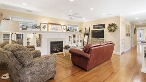 A living room with a fireplace, a television, and a ceiling fan. - 13th Street Retreat by Avantstay Ensuite Suites + Sun Porch & Patio Downtown Paso Robles (Paso Robles)