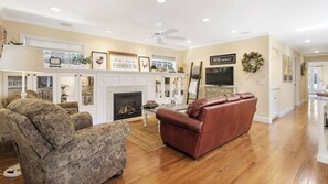 A living room with a fireplace, a television, and a ceiling fan. - 13th Street Retreat by Avantstay Ensuite Suites + Sun Porch & Patio Downtown Paso Robles (Paso Robles)