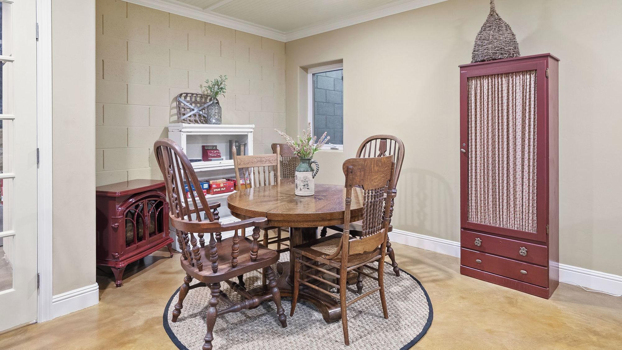 A dining area with a round wooden table surrounded by four chairs, a decorative vase with flowers, and a cabinet with a textured door.