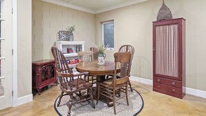 A dining area with a round wooden table surrounded by four chairs, a decorative vase with flowers, and a cabinet with a textured door. - 13th Street Retreat by Avantstay Ensuite Suites + Sun Porch & Patio Downtown Paso Robles (Paso Robles)
