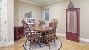 A dining area with a round wooden table surrounded by four chairs, a decorative vase with flowers, and a cabinet with a textured door. - 13th Street Retreat by Avantstay Ensuite Suites + Sun Porch & Patio Downtown Paso Robles (Paso Robles)