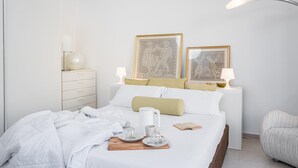 Una cama bien tendida con una bandeja de alimentos para el desayuno, una mesita de noche con una lámpara y dos cuadros en la pared.