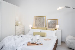 Ein ordentlich bezogenes Bett mit einem Frühstücksbrettchen, ein Nachttisch mit Lampe und zwei gerahmte Bilder an der Wand.