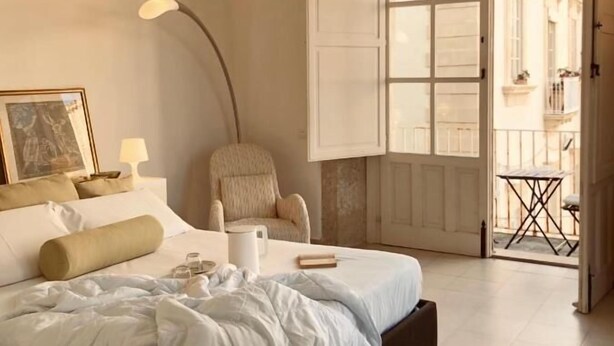 Un dormitorio con una cama, una silla, una lámpara y una puerta que da a un balcón al aire libre.