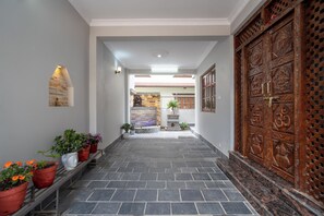 A hallway with a stone floor, a wooden door with intricate carvings, and a small Buddha statue on the left. - Serenova Apartment,  Modern 2BHK, Valley View (Kathmandu)
