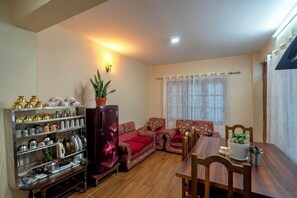 A living room with a sofa, a dining table, a refrigerator, and a shelf with kitchenware. - Serenova Apartment,  Modern 2BHK, Valley View (Kathmandu)