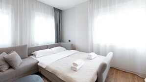 Una camera d'albergo moderna con un letto grande, un divano e tende leggere.