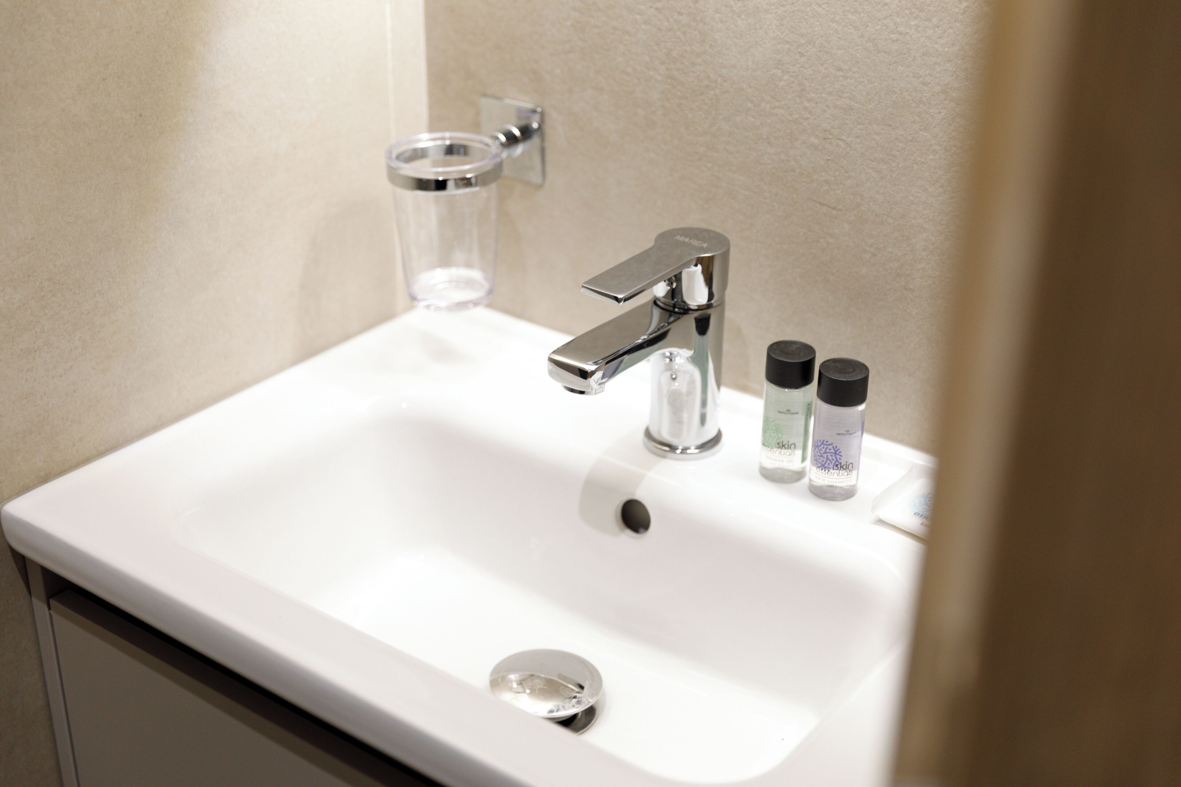 Ein weißes Waschbecken mit Armatur aus Chrom, einem Glas-Seifenspender und zwei kleinen Shampoo-Flaschen.