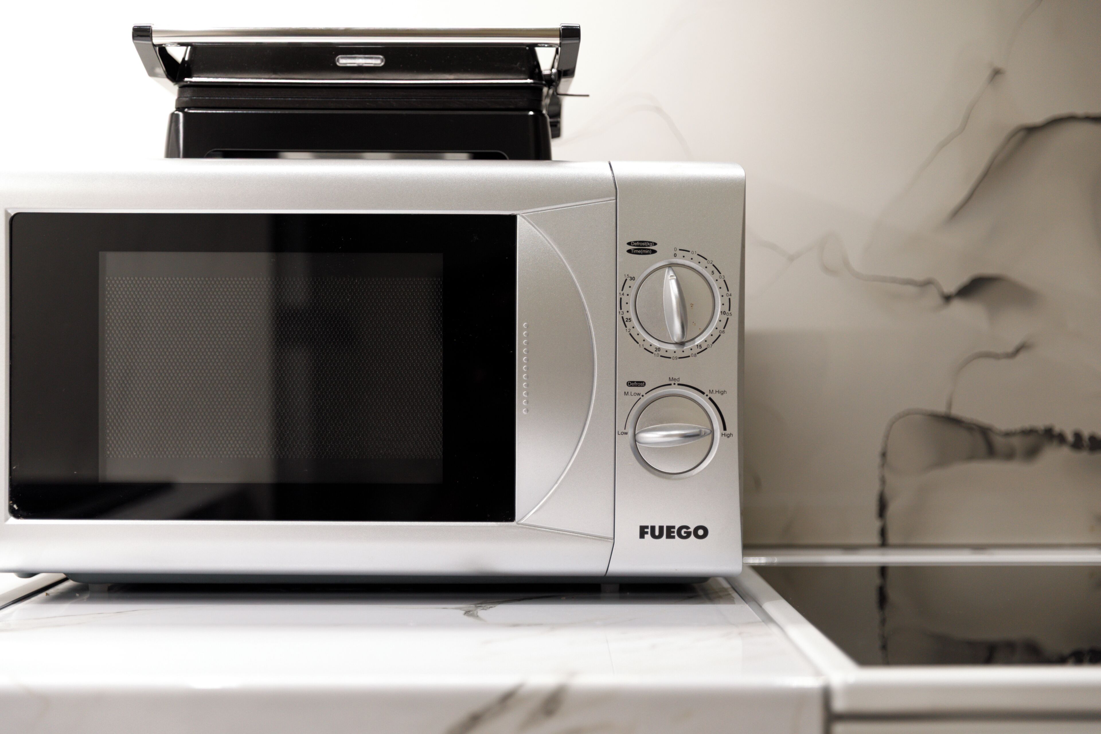 A microwave oven with a digital display and control knobs, placed on a white countertop.