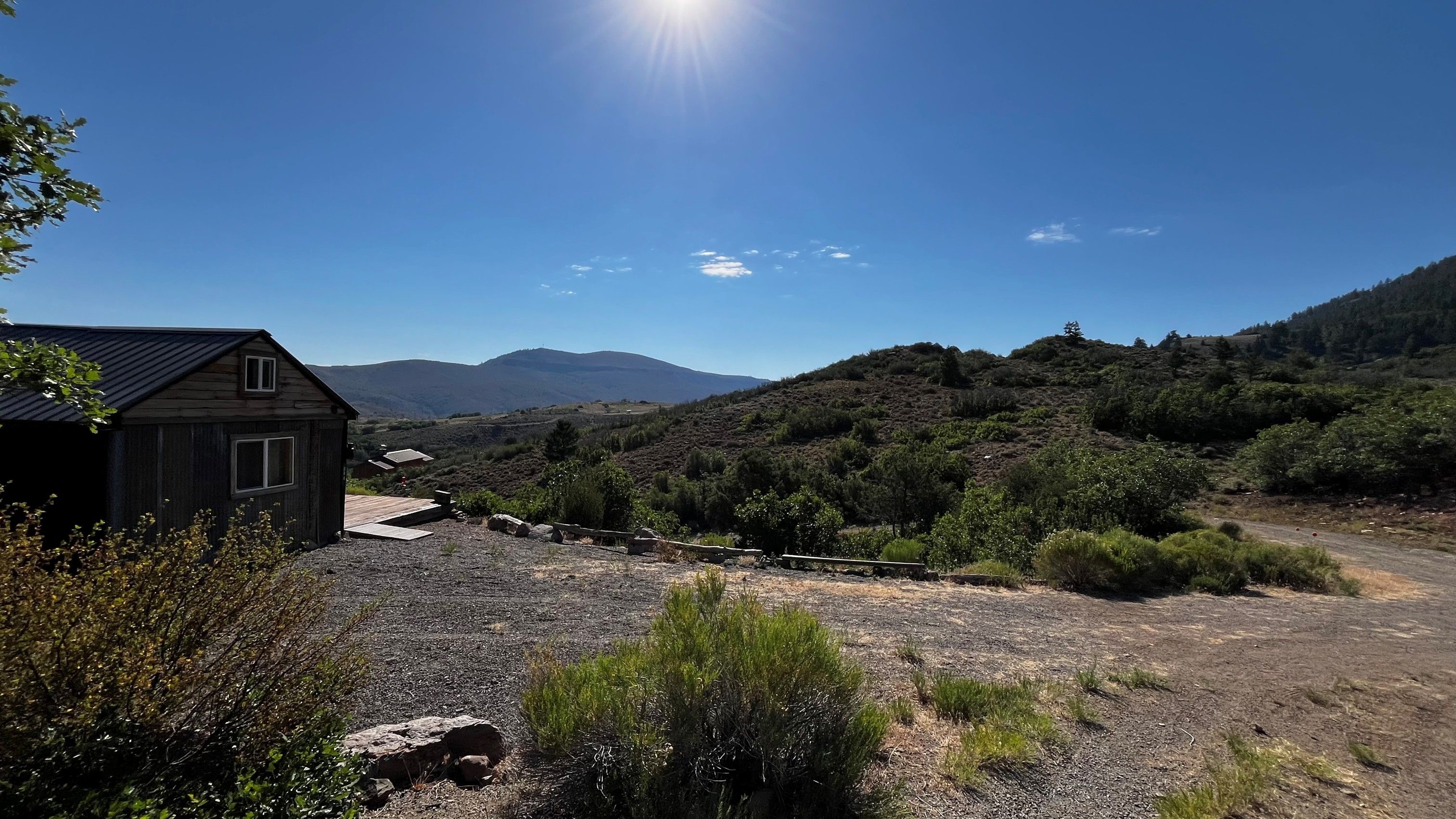 A rustic cabin with a gravel driveway and a view of a mountainous landscape.