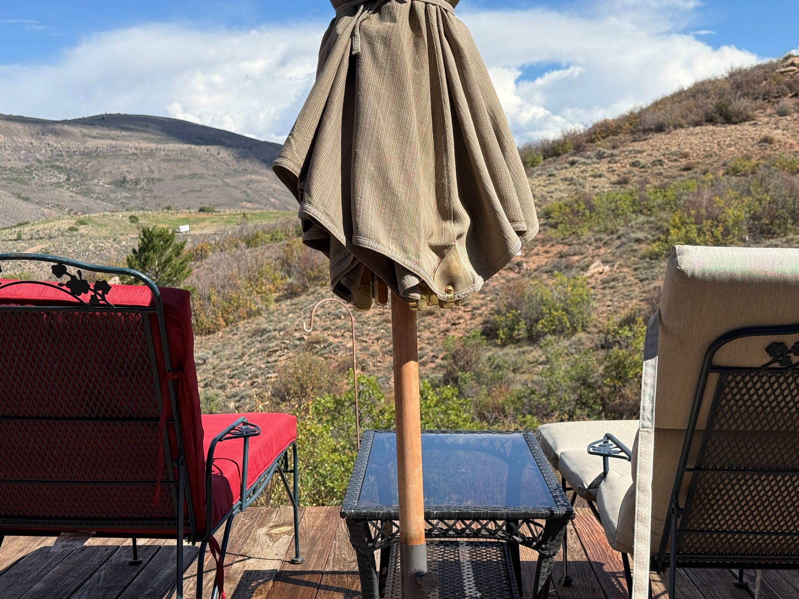 Uma área de camping com mesa e cadeiras, um guarda-sol e vista para uma paisagem montanhosa.