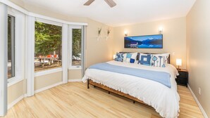 Un dormitorio con cama, ventilador de techo, ventana con vistas al exterior y un cuadro en la pared.