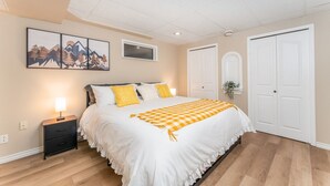 Un dormitorio con cama, mesitas de noche, una ventana y una puerta.