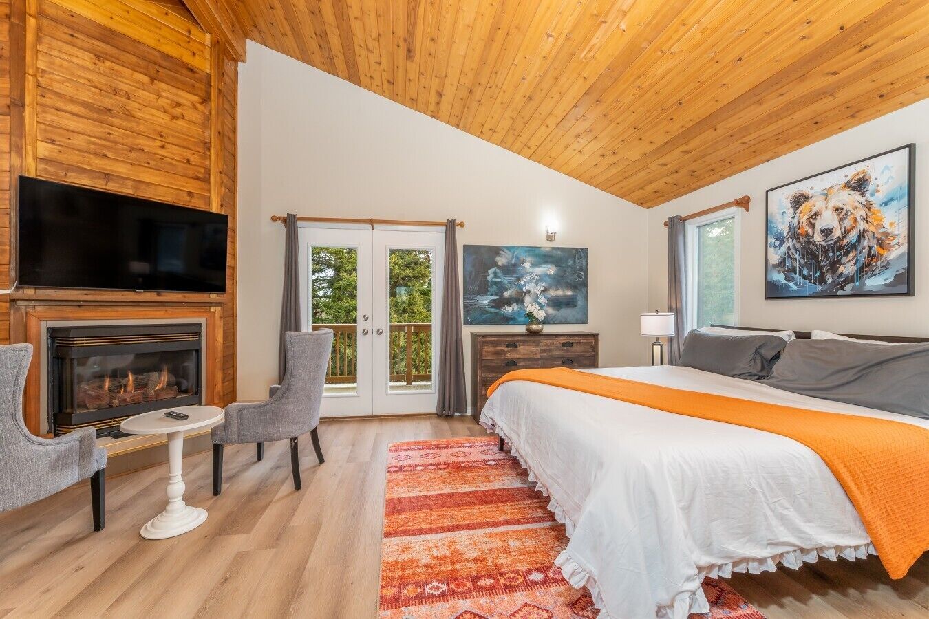 A bedroom with a fireplace, a bed, a TV, and a painting.