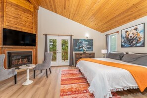 A bedroom with a fireplace, a bed, a TV, and a painting.