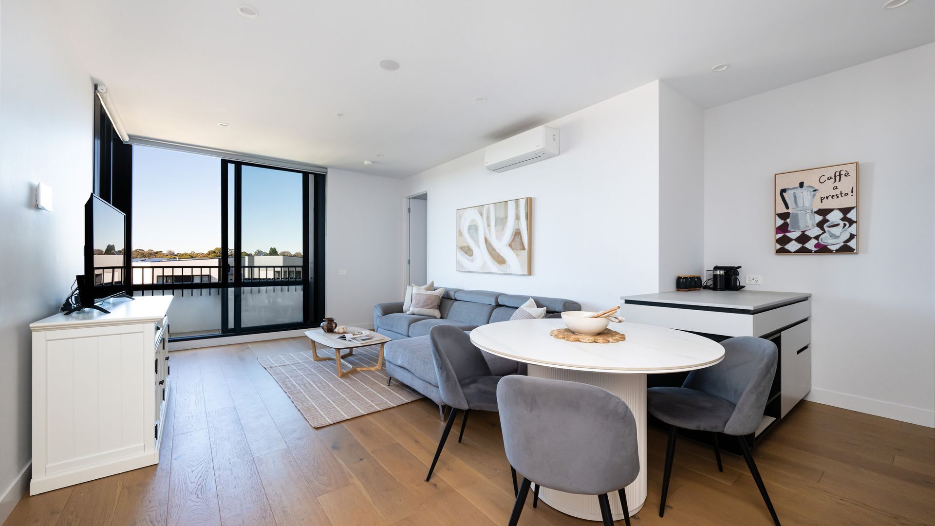 A modern living room with a sofa, a dining table, and a kitchen area.