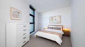 Een slaapkamer met een bed, nachtkastjes, een dressoir en kunst aan de muren.