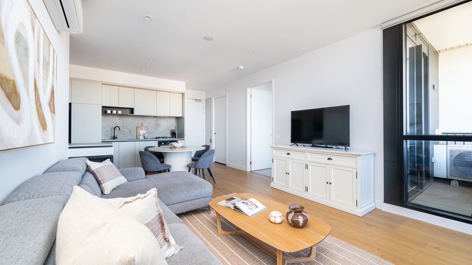 Ein modernes Wohnzimmer mit grauem Sofa, einem Holztisch und einem Fernseher auf einem Schrank.