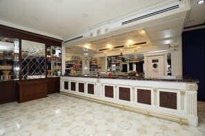 Angolo bar con un bancone in marmo, scaffali con bottiglie e un soffitto decorativo.