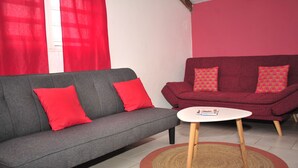 Ein Wohnzimmer mit einem grauen Sofa und einem roten Sessel, beide mit passenden roten Kissen. Vor dem Sessel steht ein kleiner weißer Tisch mit einem Buch.