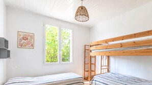 Ein Zimmer mit zwei Etagenbetten, einem Fenster mit Blick auf Grünflächen, einer hängenden Leuchte und einem gerahmten Bild an der Wand.