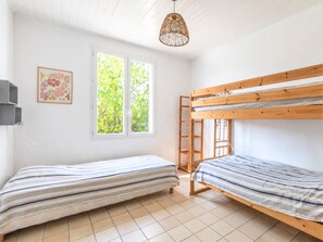 A room with two bunk beds, a window with a view of greenery, a hanging light fixture, and a framed picture on the wall. - La Linière - Proche plage - Petfriendly (Noirmoutier-en-l'Île)