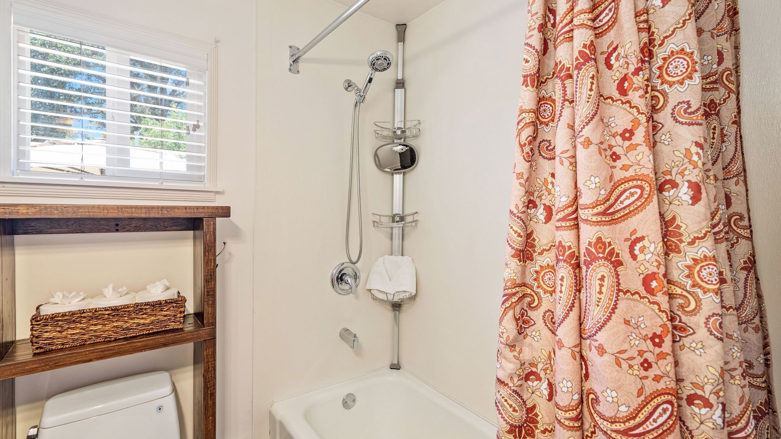 A bathroom with a shower, a bathtub, a window with blinds, and a patterned curtain.