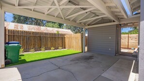 Ein überdachter Patio-Bereich mit Betonboden, Holzzaun und Rasenfläche.