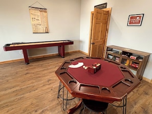 A room with a pool table, a dartboard, and a card game table.