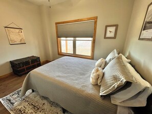 A bedroom with a large bed, a window with blinds, a map on the wall, and a suitcase.