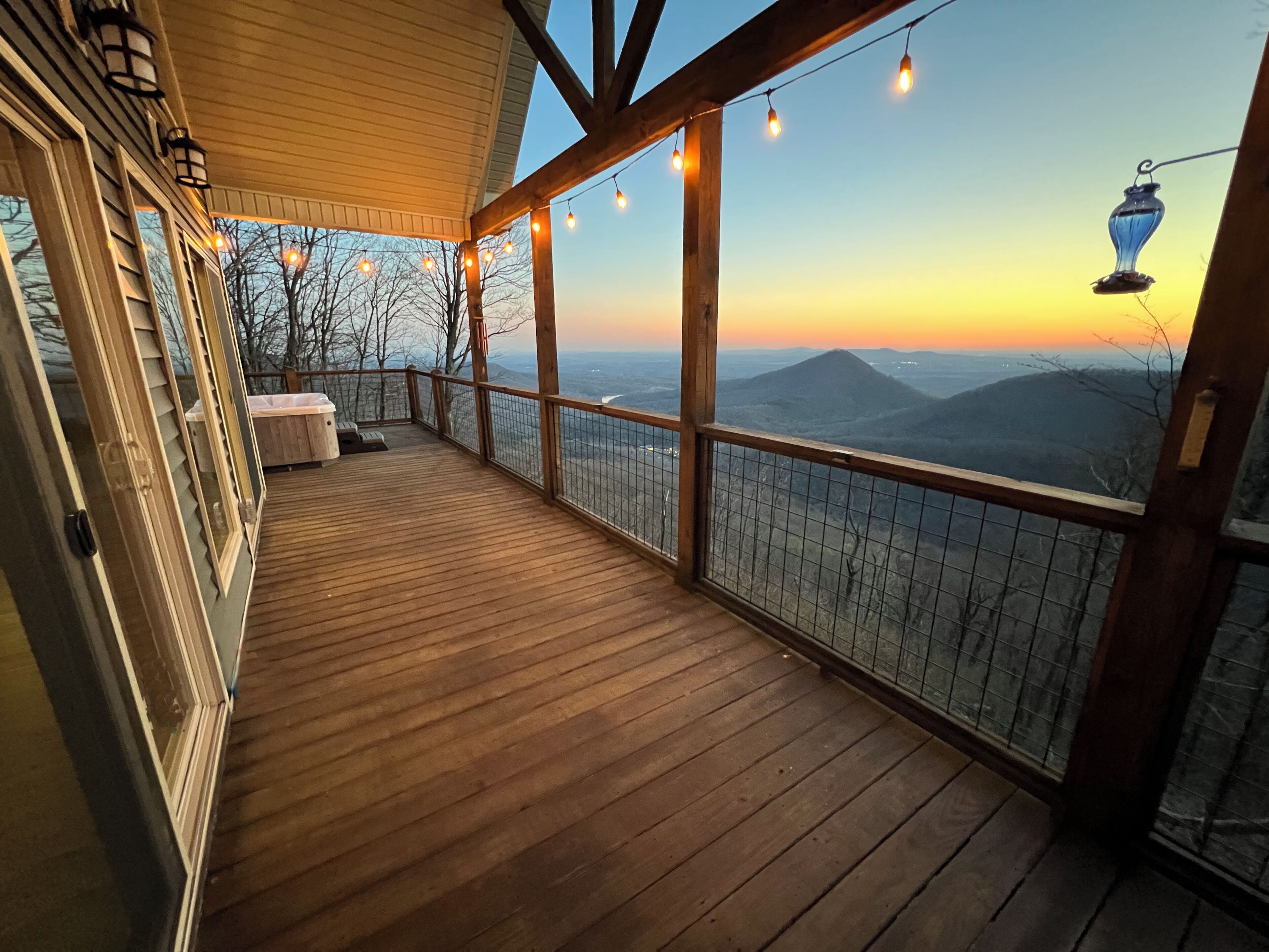 A wooden deck with a view of mountains, a railing, and string lights.
