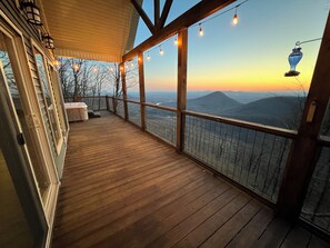 A wooden deck with a view of mountains, a railing, and string lights.