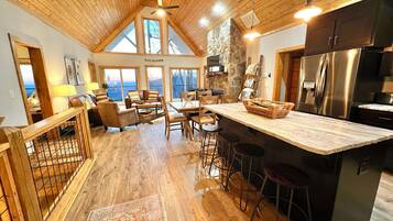 A spacious living area with a high ceiling, wooden flooring, and a large island with stools.