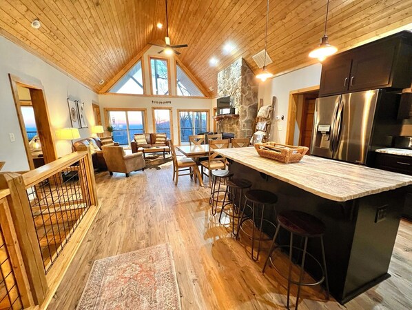 A spacious living area with a high ceiling, wooden flooring, and a large island with stools.