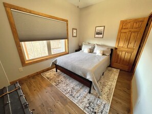 Un dormitorio con un ventanal grande, una cama con colcha estampada, una mesita de noche y un armario de madera.