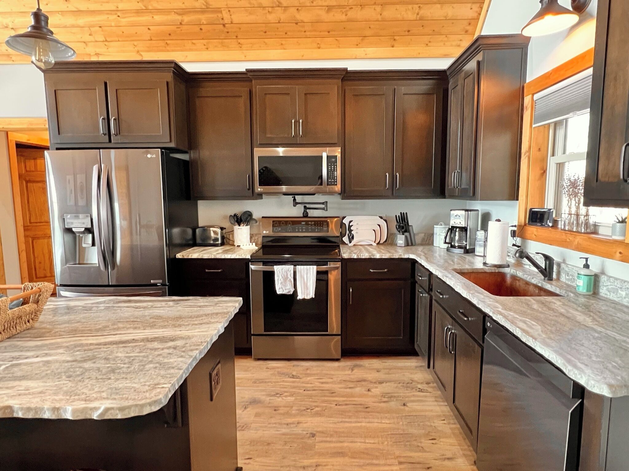 A modern kitchen with dark wood cabinets, stainless steel appliances, and a marble countertop.