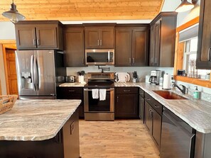A modern kitchen with dark wood cabinets, stainless steel appliances, and a marble countertop.