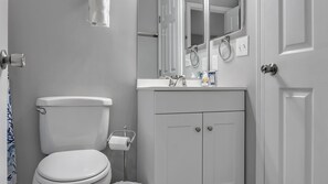 A bathroom with a toilet, a sink with a mirror above it, and a cabinet below.