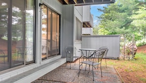 A patio with a table and chairs, a sliding glass door, and a view of trees.