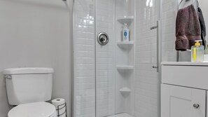 A bathroom with a toilet, a shower stall, a sink, and a towel rack.