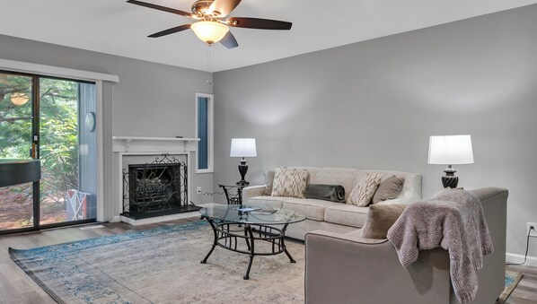 A modern living room with a fireplace, a glass coffee table, a sofa, and two lamps.
