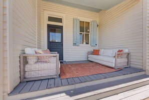 Eine Veranda mit zwei Korbstühlen, einem weißen Sofa und einem roten Teppich.