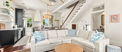 A modern living room with a sectional sofa, a round coffee table, and a staircase leading to the upper floor.